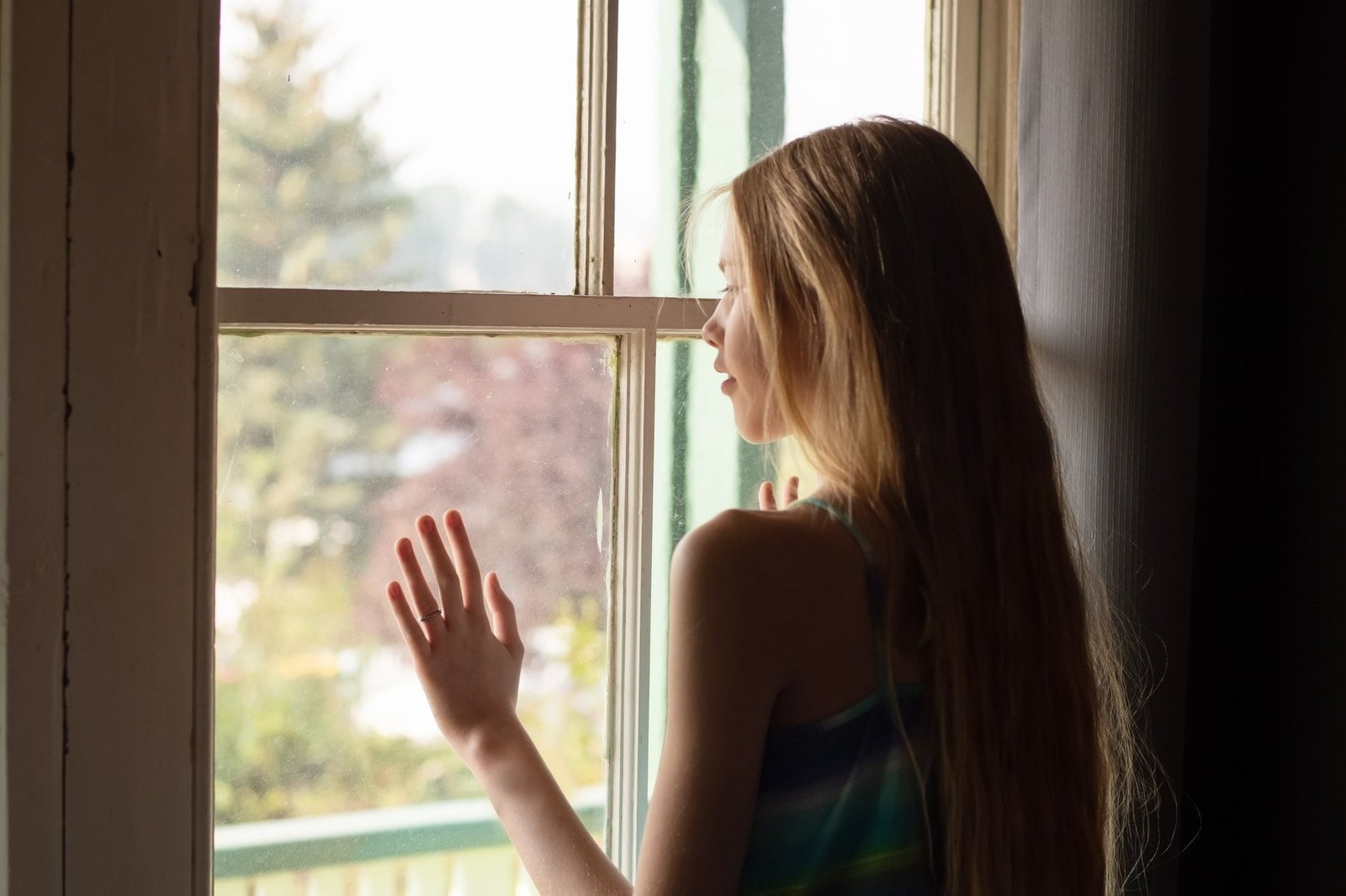 Teenage girl looking through the window. Self isolation. Reflection